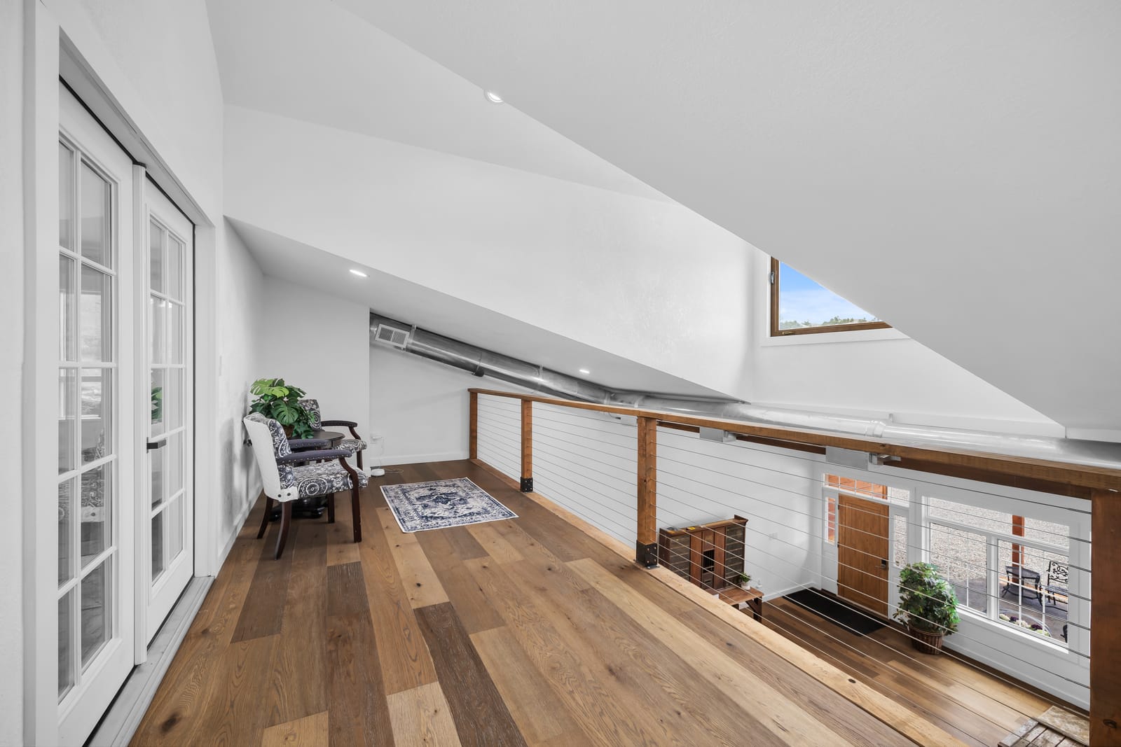 Quiet loft lounge with a reading chair and wood floors overlooking the main living area at New Frontier Recovery Center in Huntley, Montana